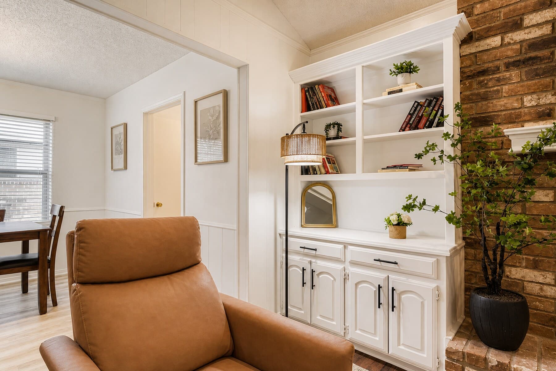 Cozy seating nook with a white built-in bookshelf, styled decor, and a brick accent wall.